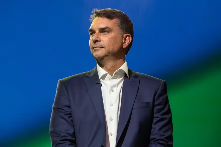 Flávio Bolsonaro em estúdio, com fundo azul e verde